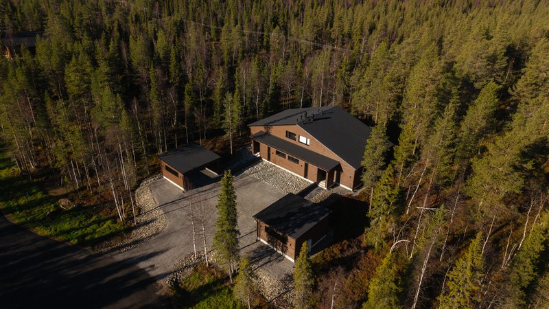 Villa Löhö from the air in autumn sunshine: the drive leading up between two carports to the building, surrounded by forest.