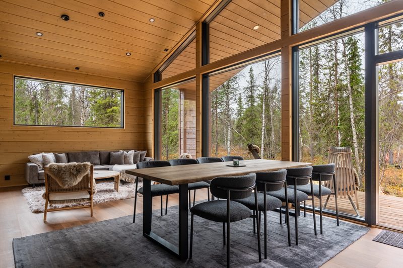 The open living and dining room with a wall of glass onto the deck, a long table for eight and sheepskins on the sofa.