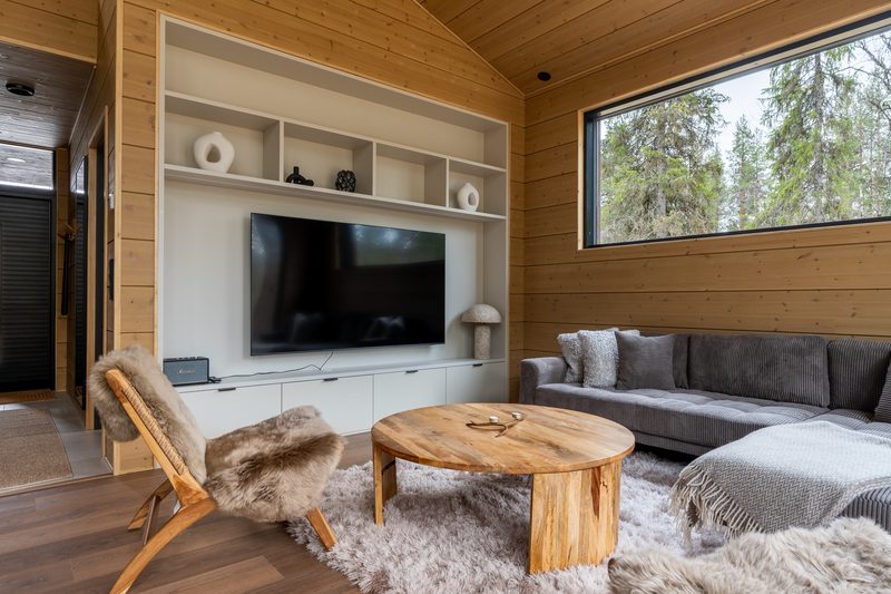 The living room from the other end: television, open shelving, sofa and a sheepskin-draped chair.