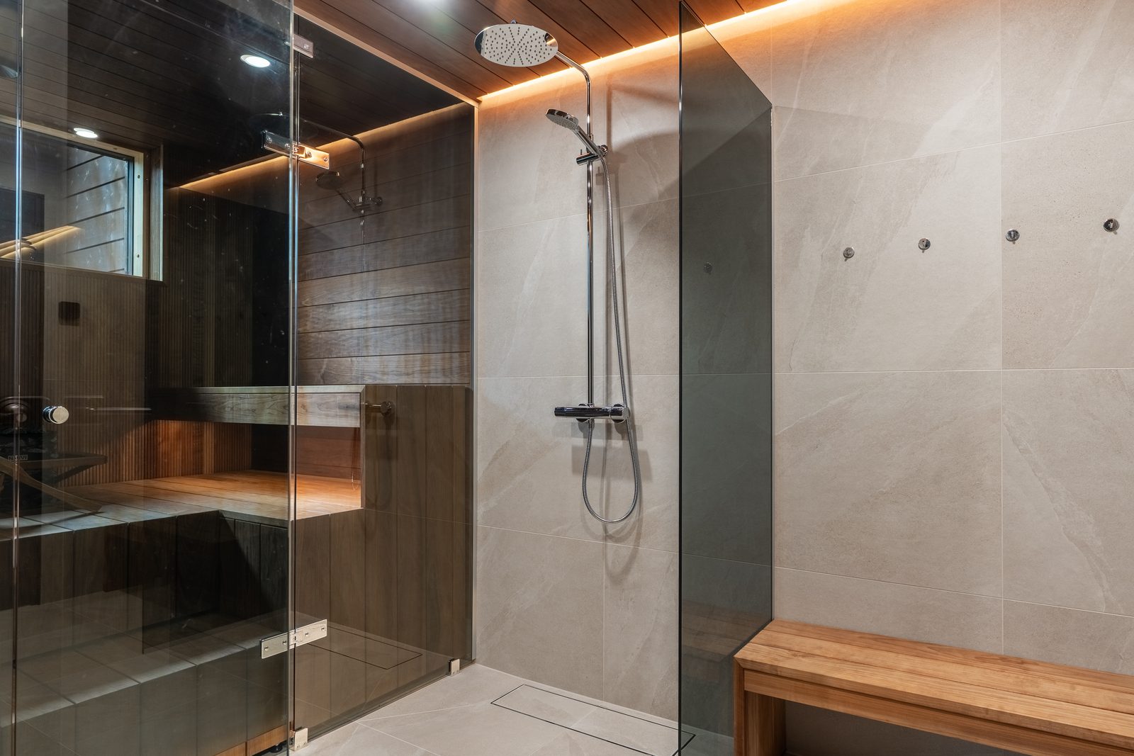 The washroom: a rain shower behind glass, stone-effect tiles, and the sauna visible through the glass wall.